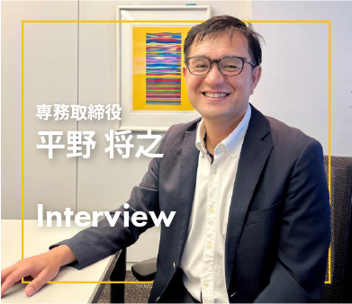 笑顔でインタビューに応じる専務取締役・平野将之氏がオフィスで座っている様子