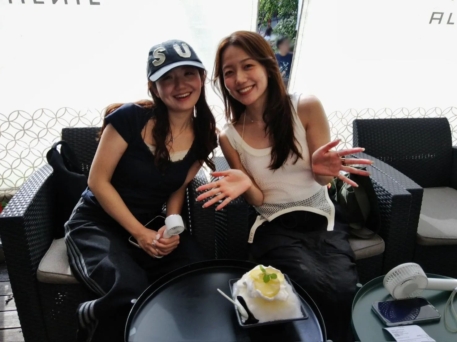 カフェのテラス席で笑顔で並ぶ2人の女性